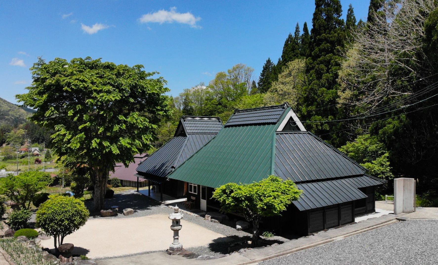 旅館 吉和の風 — 母屋外観 · 入母屋の大屋根と杉の高木に囲まれた山あいの古民家