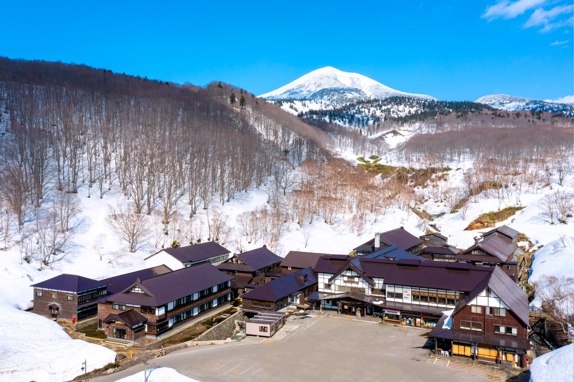 酸ヶ湯温泉旅館 — 青森・八甲田 · 残雪の八甲田連峰を背にした木造の一軒宿の全景