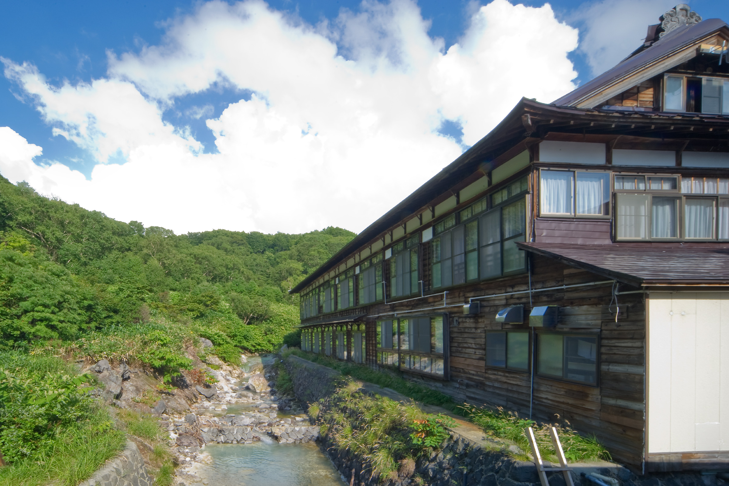 酸ヶ湯温泉旅館 — 青森・八甲田 · 沢沿いに連なる木造二階建ての湯治棟と夏の渓流
