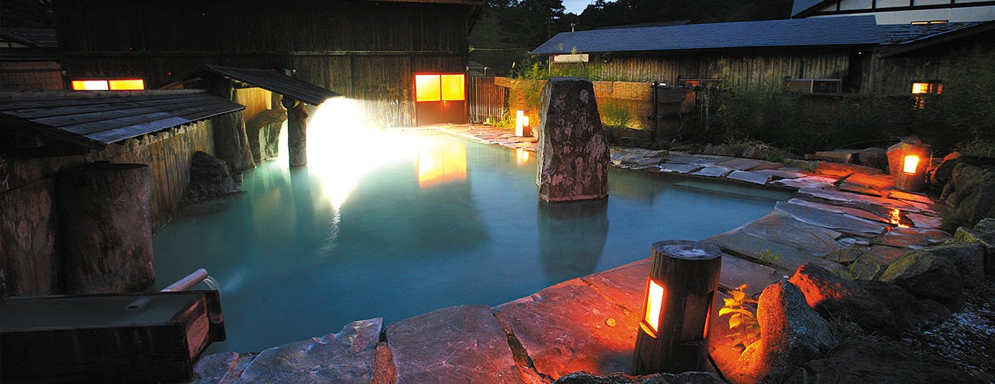 泥湯温泉 奥山旅館 — 秋田県湯沢市 · 白濁の「新湯」を注ぐ男女別大露天風呂、暮れかけの山肌と灯り