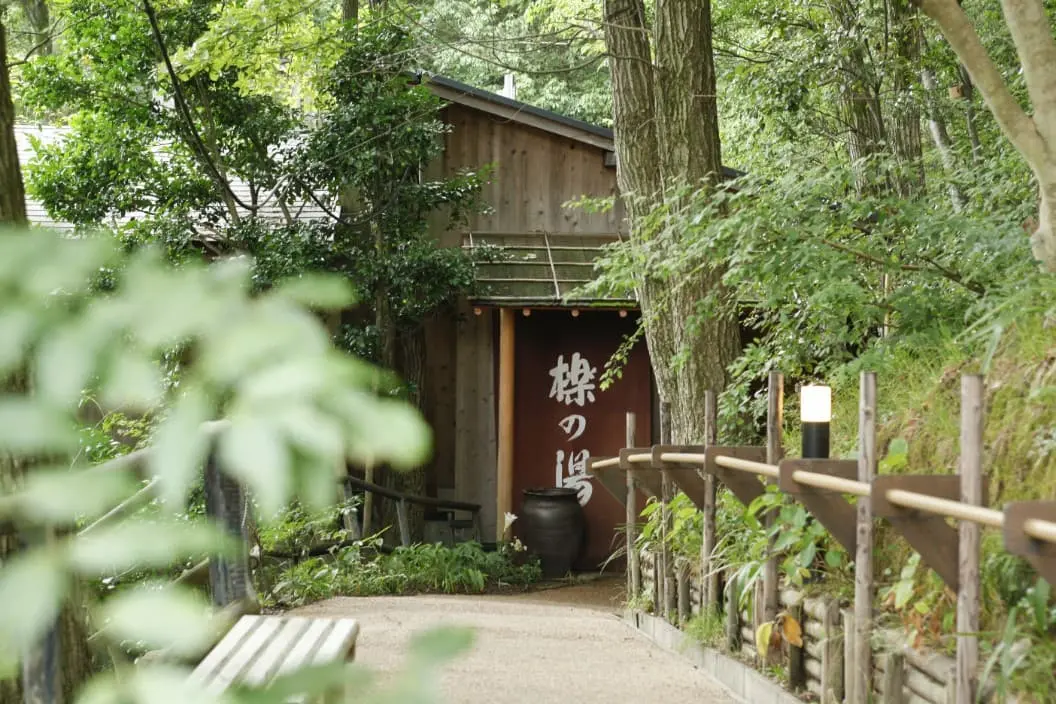 銀水荘 兆楽 — 神戸市北区有馬町 · 杉林の斜面に建つ板張りの湯屋と、玉砂利敷きのアプローチ