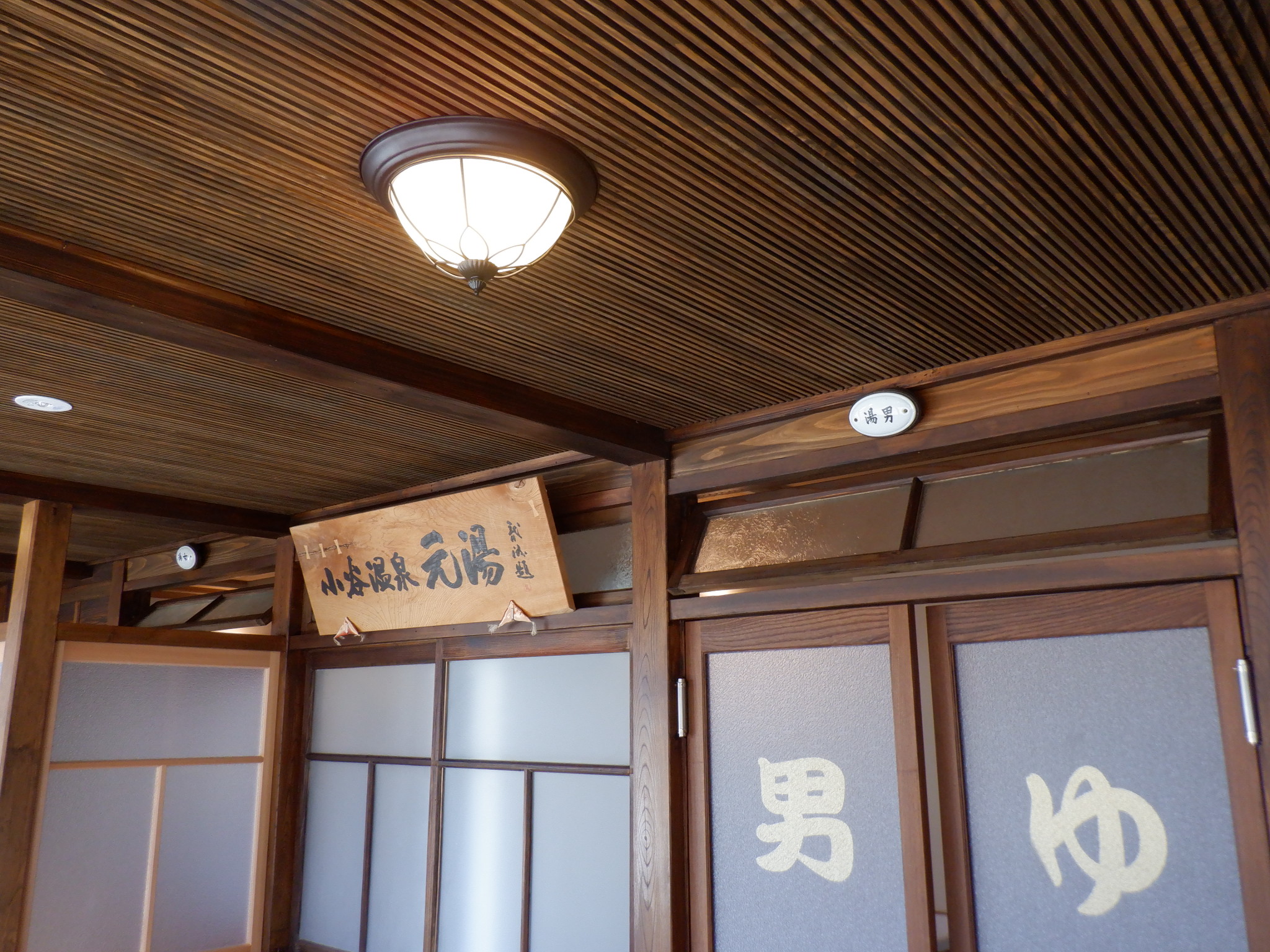 小谷温泉 山田旅館 — 長野県小谷村中土 · 「小谷温泉 元湯」の扁額を掲げた浴室棟の入口と木の天井