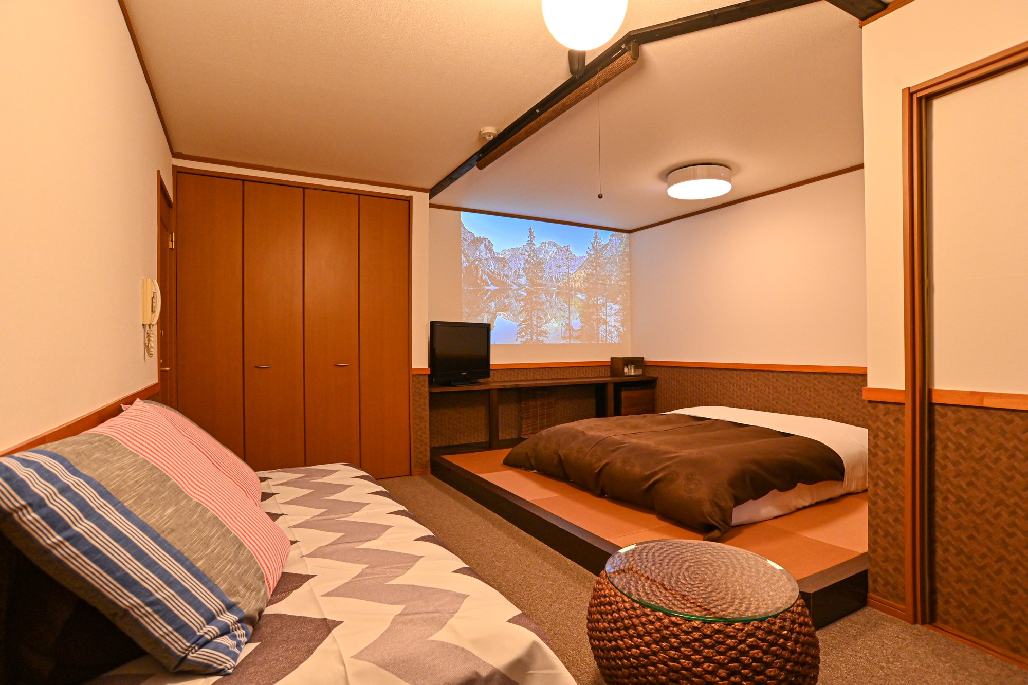 Lakeside Inn Beehive — 福島県北塩原村・裏磐梯 · 小上がりの畳にベッドを据えた和洋室、投影用の白壁を備える