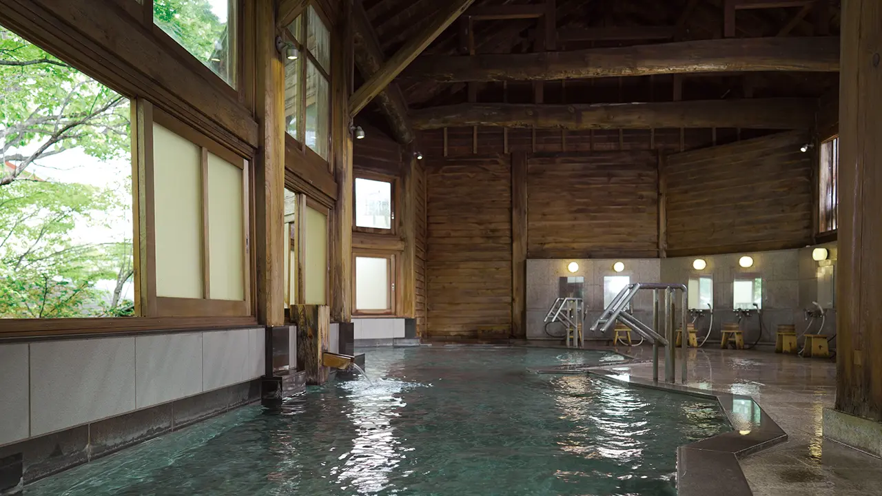 草津温泉 望雲 — 群馬・草津町 · 丸太梁の木造の小屋組みと石張りの湯船を持つ大浴場「万代の湯」
