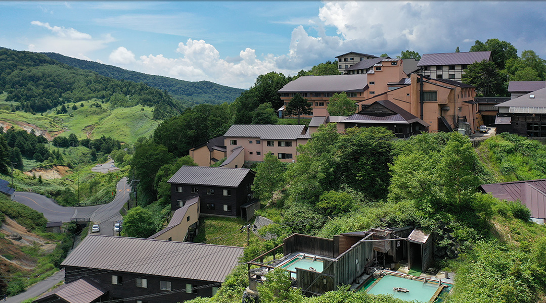 万座温泉 日進舘 — 群馬・嬬恋村 · 斜面に建つ館と木の囲いを持つ露天風呂「極楽湯」の俯瞰